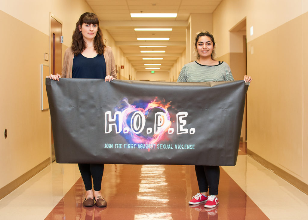 Francesca Valencia (right), sociology and theatre major, and founder of the organization H.O.P.E., holds the club banner with the club adviser and English professor, Bridget Kominek. Photo credit: Sue Hwang