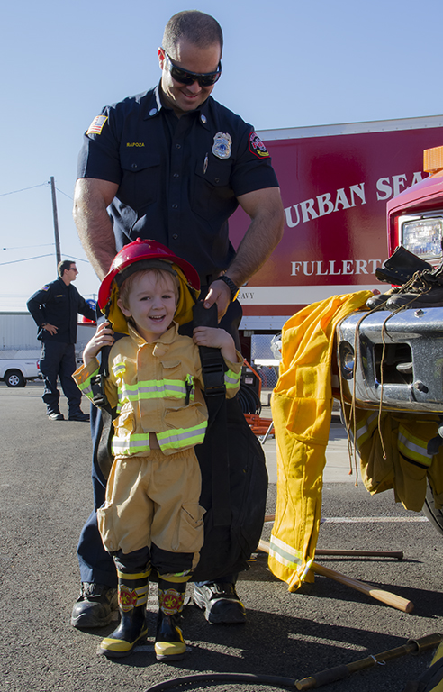Jr firefighter trying on some of the gear with the help of Firefighter Rapoza at the Fullerton Fire Dept. Pancake Breakfast in Fullerton on 11-7-15 Photo credit: Neddie Facio