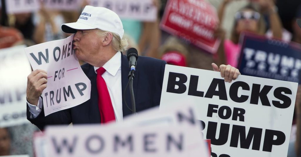Trump at a rally holding up signs, Women for Trump and Blacks for Trump. Photo credit: Digg.com