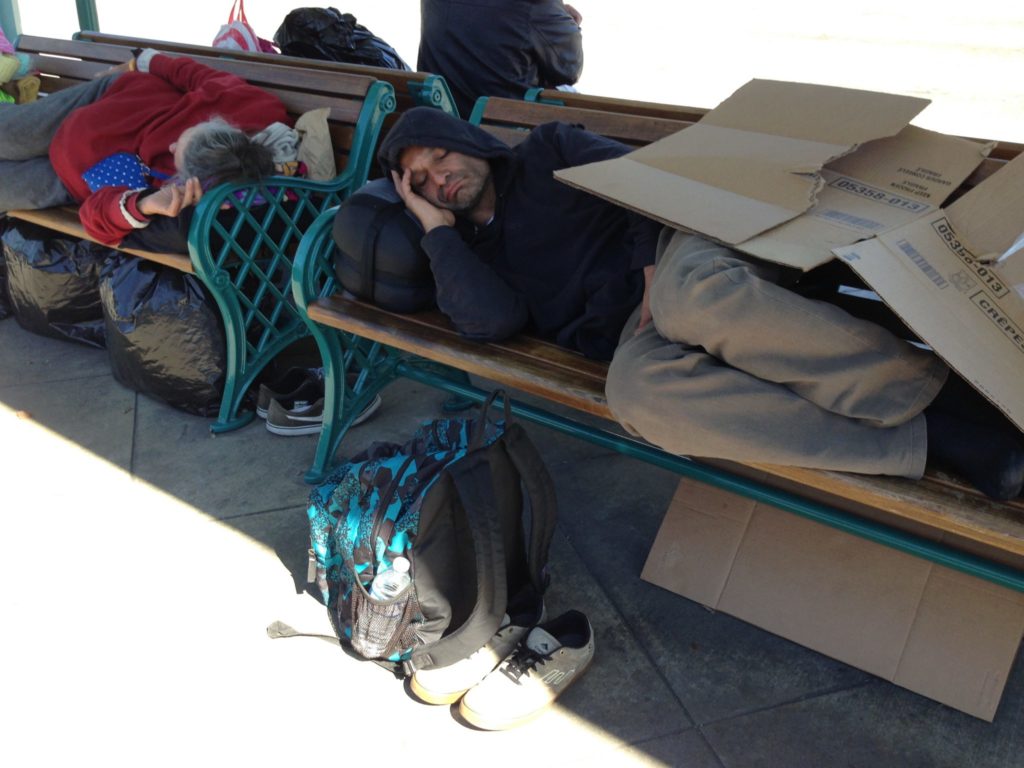 Two individuals sleeping on a bus stop bench in Anaheim. Photo credit: Cristal Ruiz