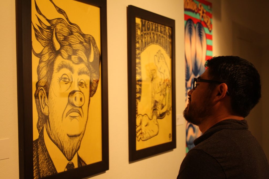 Narsiso Martinez, one of the four artists of the exhibit, examines Devil Piggy Trump by artist Gomez Bueno. Photo credit: Aaron Untiveros