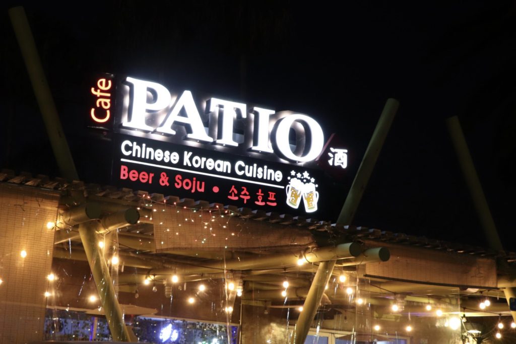 Above the outdoor seating area, an illuminated sign displays the restaurants full name: Cafe Patio Chinese Korean Cuisine. Photo credit: Jocelyn Rabadan