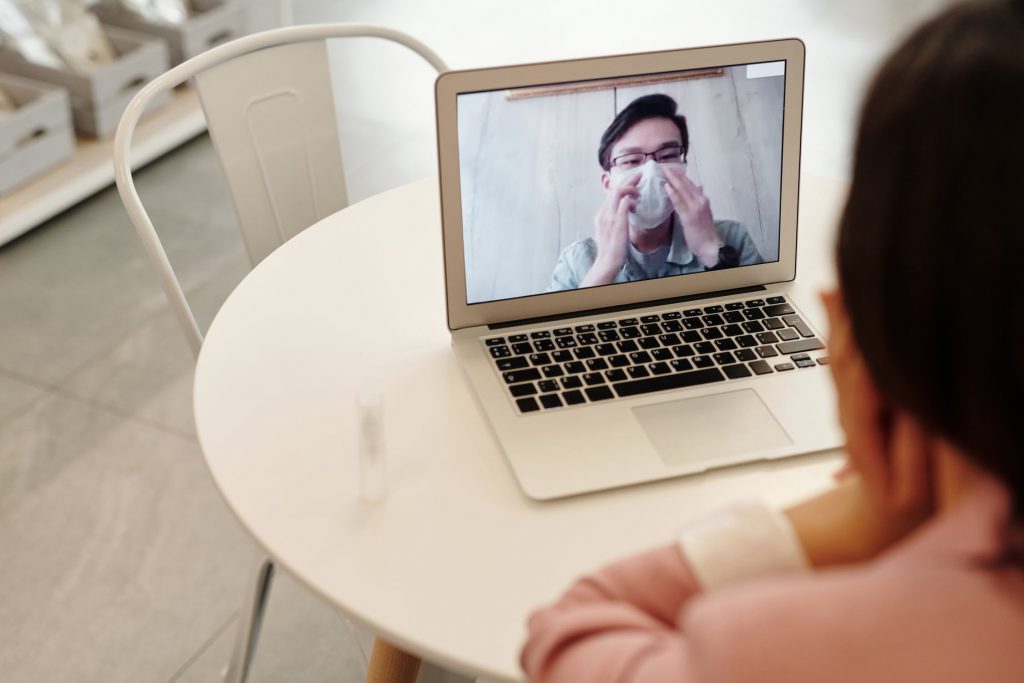 A woman video chats with a man wearing a surgical mask.
