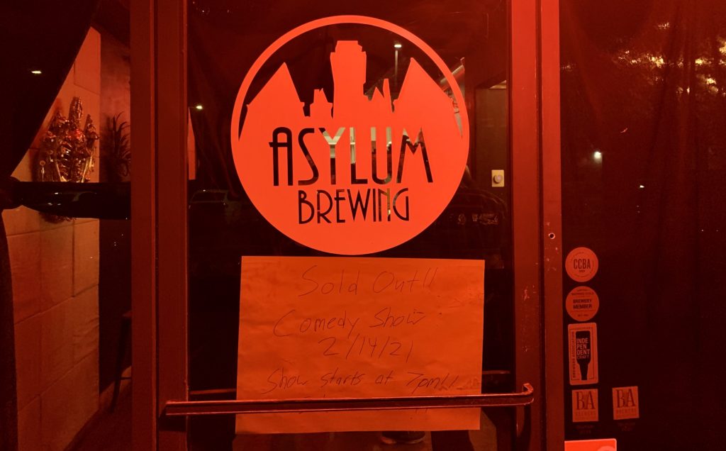 Asylum Brewing has a red lit entrance with a handwritten note that the comedy show sold out. Photo credit: Rachel Lopez