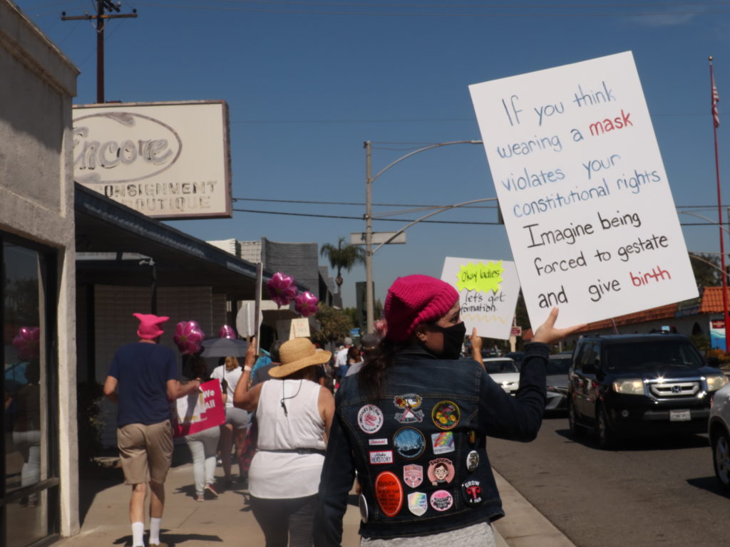 Whittier resident Fallon Foy marched with her sign, refuting mask mandates as unconstituional in comparison to women forced into unwanted pregnancy. Photo credit: Rachel Lopez