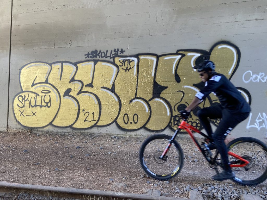 Mountain biker passing through the graffiti filled Harbor Boulevard underpass along the Fullerton Loop Trail. Photo credit: Dustin Malek