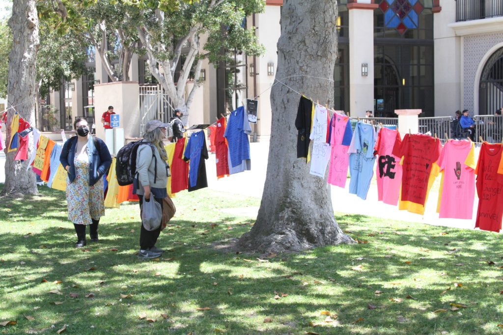 People in passing reading some of the stories on the shirts at April 19 Clothesline Project.    
  **(*WHERE is this?) Photo credit: Valerie Strummer