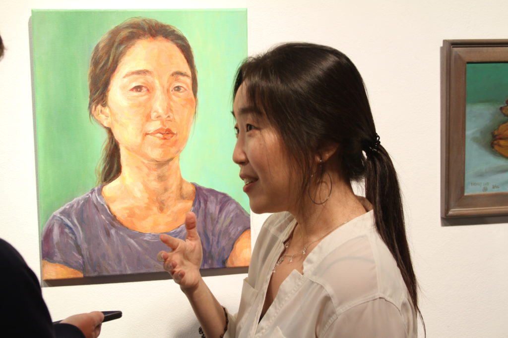 Rhia Kang, FC student, chats in front of her self-portrait, the winner of an award in painting at the 2022 Student Art Exhibition, currently on display at the FC art gallery through May 11. Photo credit: Gerardo Chagolla