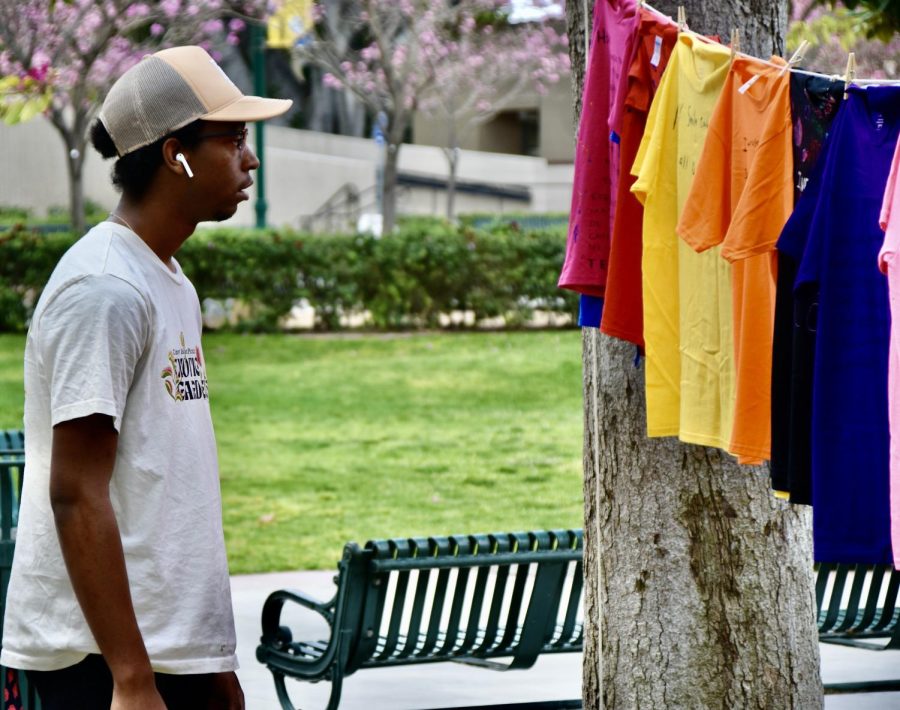 Miles Ellis, a sophomore at Fullerton College reads a t-shirt that tells the impact of The Clothesline Project, on Tuesday, April 18, 2023. Photo credit: Gerardo Chagolla