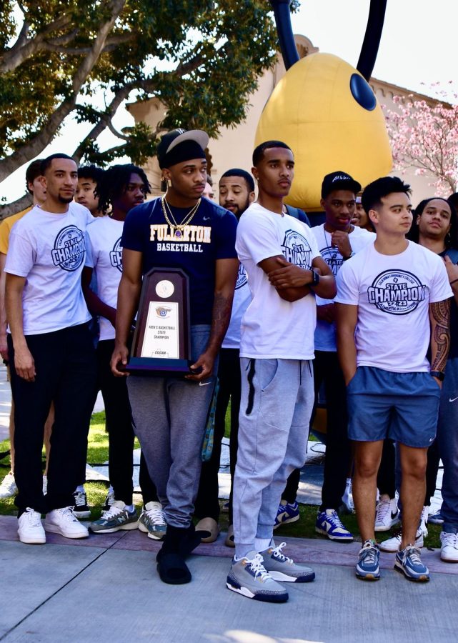 Freshman forward Jeremiah Davis holds the CCCAA State Championship trophy with Buzzy, freshman guard Sean Newman Jr., sophomore guard Kobe Newton, assistant coach Kaipo Villeza, and others at the celebration of the Hornets Men's Basketball team winning the state title on campus on Thursday, April 6, 2023.