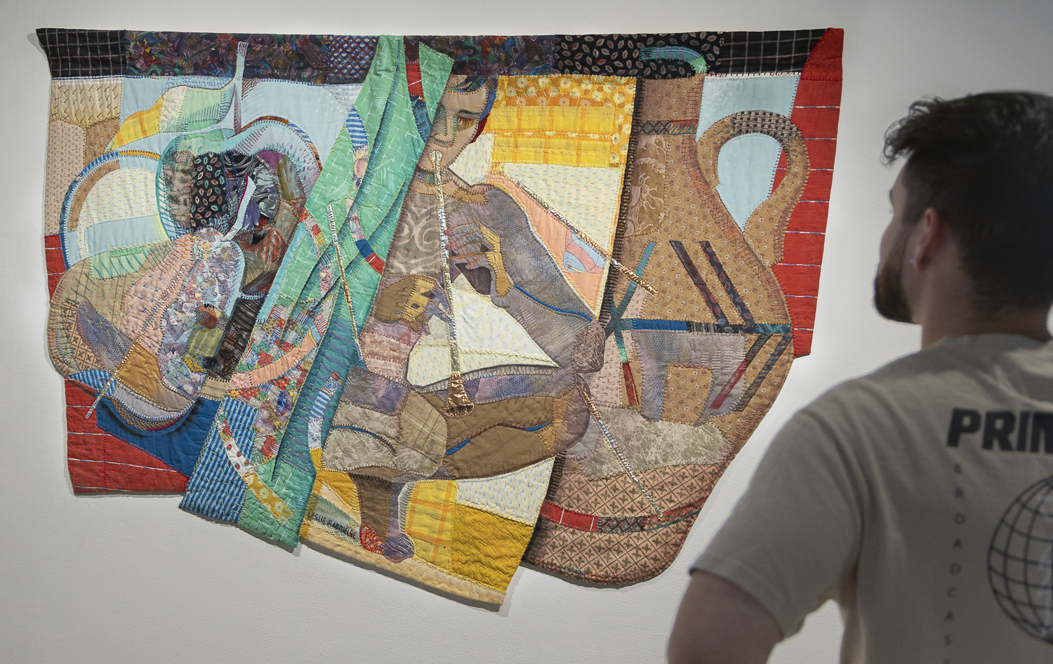 An attendee of the opening night of The Dark Room: Selections from the Fullerton College Collection admires the fabric appliqué work of Leslie Gabrielse in her piece, The Flute Player, circa 1992.