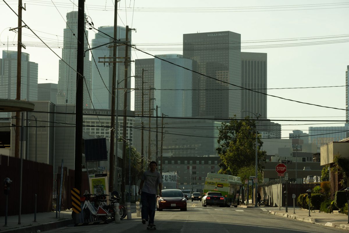 Jonah Delgado riding his skateboard down a street with downtown buildings behind him.